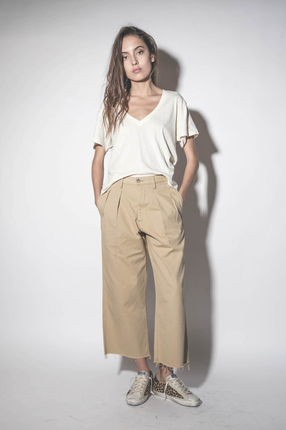 Pantalon large à pinces en toile de coton beige Chino Denimist. Porté les mains dans les poches.